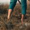 man wading barefoot in a wetland with a spade